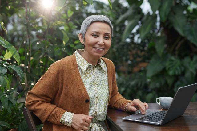 Elderly woman in brown sweater using computer and smiling