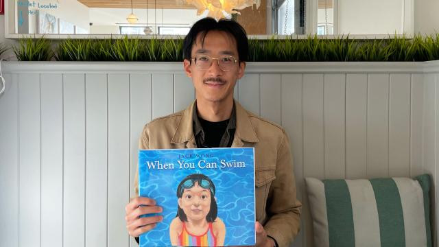 Photograph of author/illustrator Jack Wong holding a copy of his book When you can swim