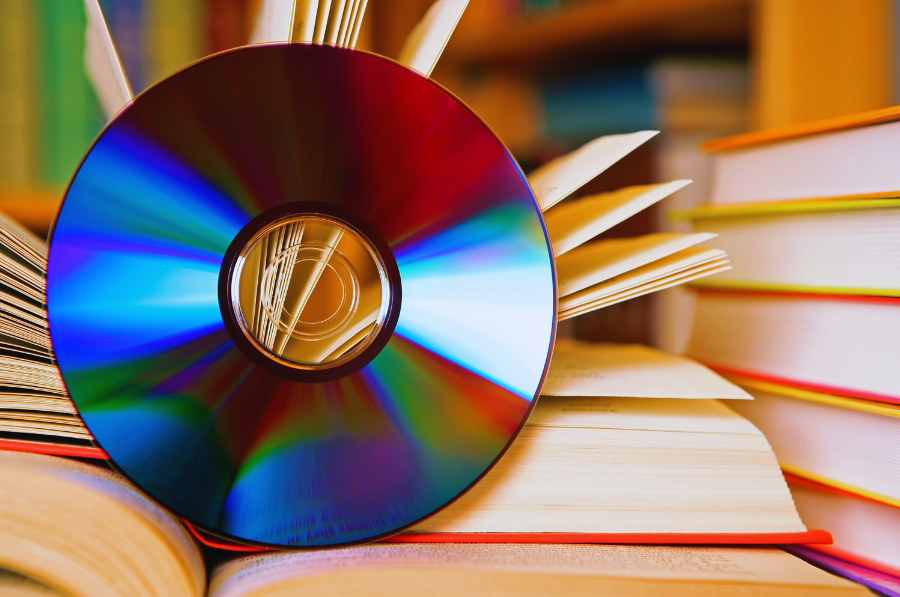 A CD is propped against an open book beside a stack of more books.