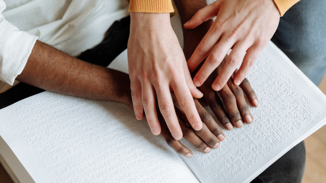 Une paire de mains en recouvre une autre sur un livre en braille ouvert.