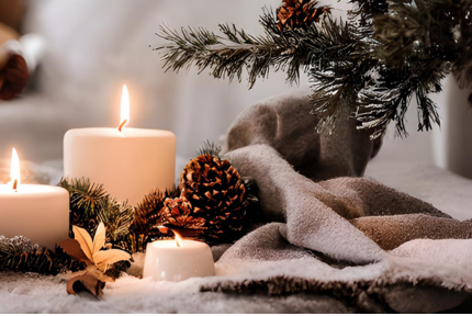 Two white lit candles are surrounded by pine branches, pinecones, and a white blanket.