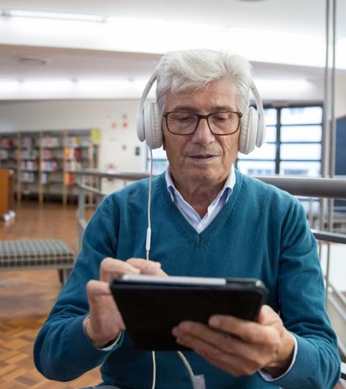 Older man wears headphones while using a tablet.