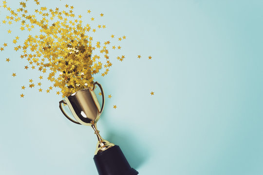 Un trophée qui déborde de confettis or sur un fond bleu.