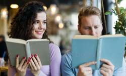A woman holding a book looks at the man seated beside her who is reading a book.