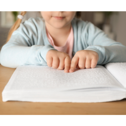 Un enfant lit un livre en braille à une table.